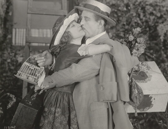 A black-and-white photograph of a White woman eagerly embracing and kissing a White man who is taken by surprise.