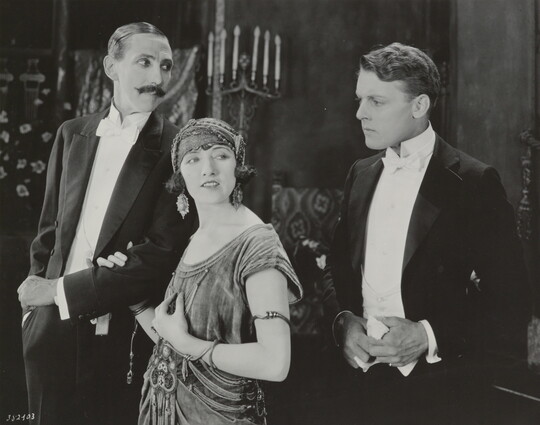A black-and-white photograph of a White woman and two White men, all dressed in formal attire and looking in different directions.