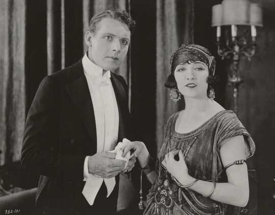 A black-and-white photograph of a White woman and a White man, both elegantly dressed and looking at something in the distance.