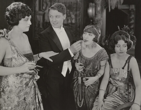 A black-and-white photograph of three White women and one White man, all elaborately dressed and engaged in conversation.