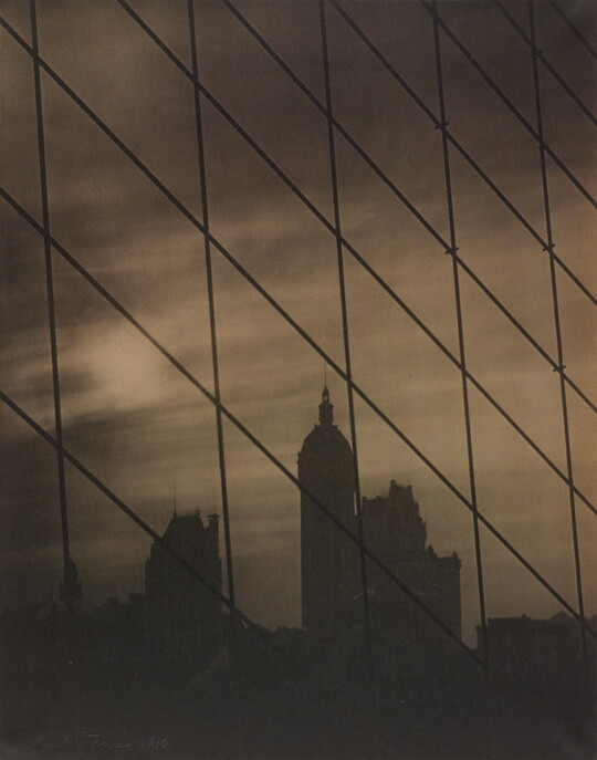 A sepia-toned photograph of a patterned grid of cables in front of a dark city skyline.