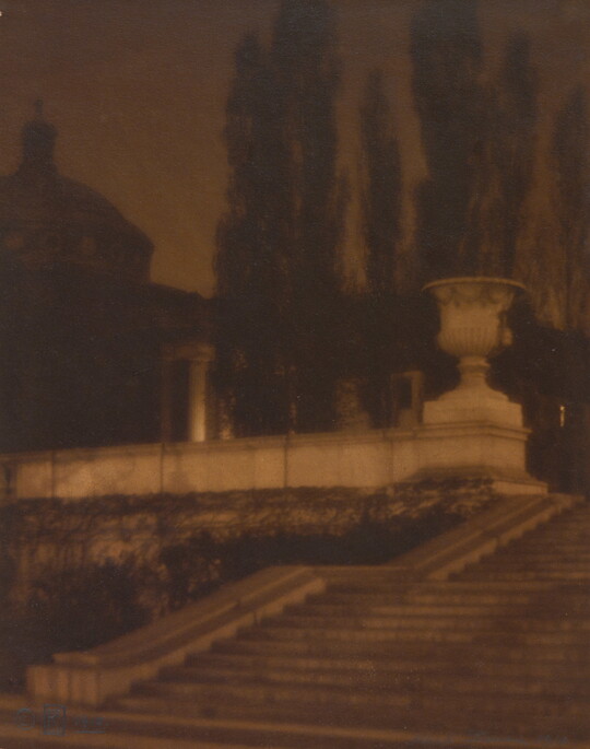 A sepia-toned photograph of a set of stone stairs leading to a plaza with a large urn, a domed building, and tall thin trees.