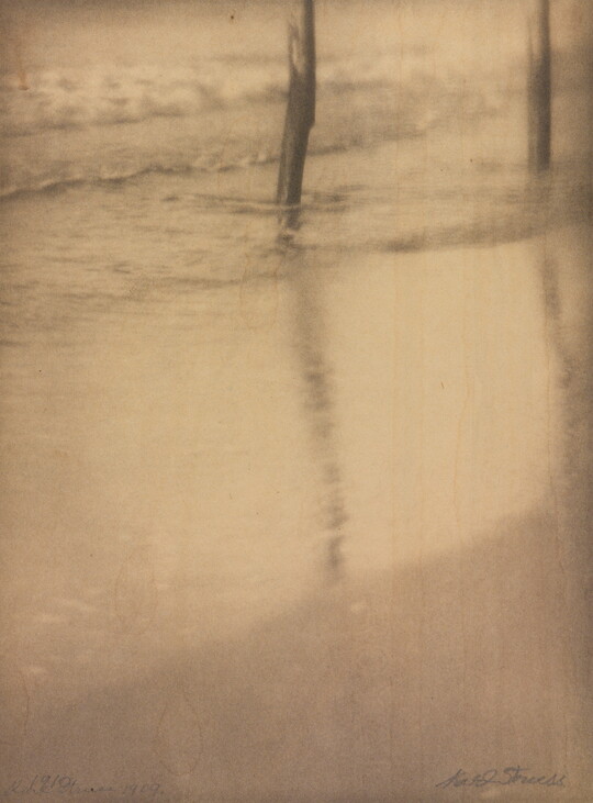 A sepia-toned photograph of water washing on a sandy beach around two poles in the top left corner.