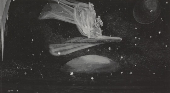 A black-and-white photograph of two White people in costume looking as if they were flying above the moon and stars.