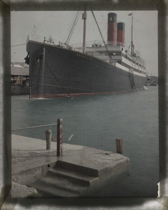 A color image large ship with red smokestacks docked in a harbor.