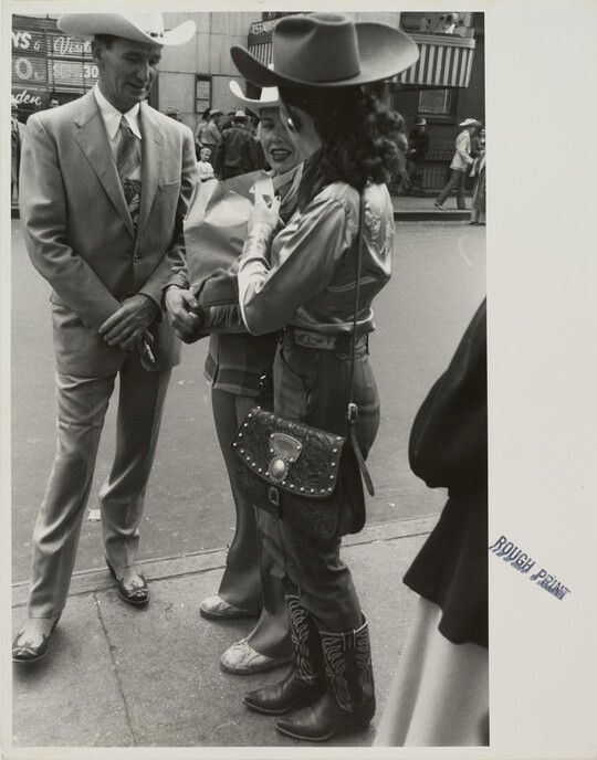 A black-and-white photograph of two women and one man, all in Western dress, talking on a busy sidewalk.