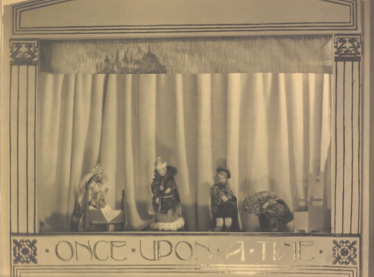 A sepia-toned photograph of a puppet stage with four puppets and the words "Once Upon a Time" written at the bottom.
