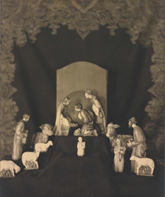 A sepia-toned photograph of human and animal figurines assembled on a black fabric background in a nativity scene.