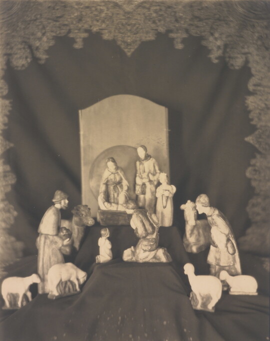 A sepia-toned photograph of human and animal figurines assembled on a black fabric background in a nativity scene.