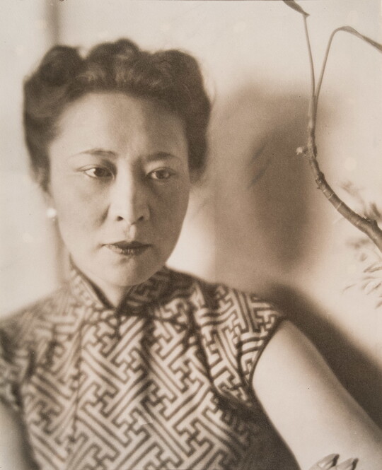A sepia-toned portrait photograph of a woman with Asian features, her hair pulled up, wearing a top with a geometric design.
