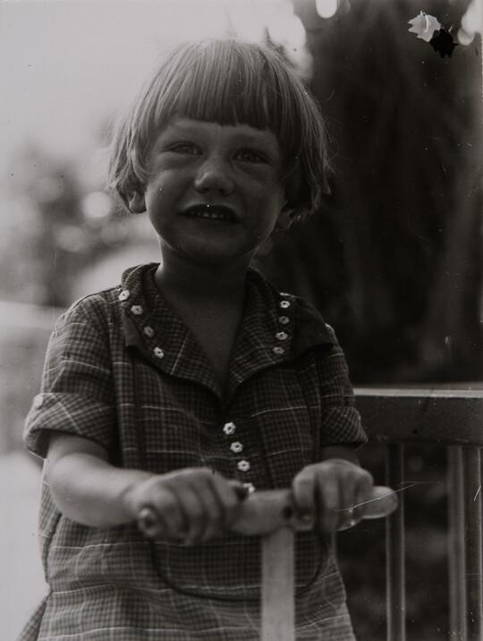 A black-and-white photograph of a young White child with short hair holding the handle of a toy of some sort.