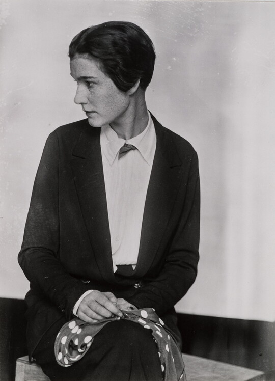 A black-and-white portrait photograph of a seated White woman holding a scarf in her lap with her head turned in profile.