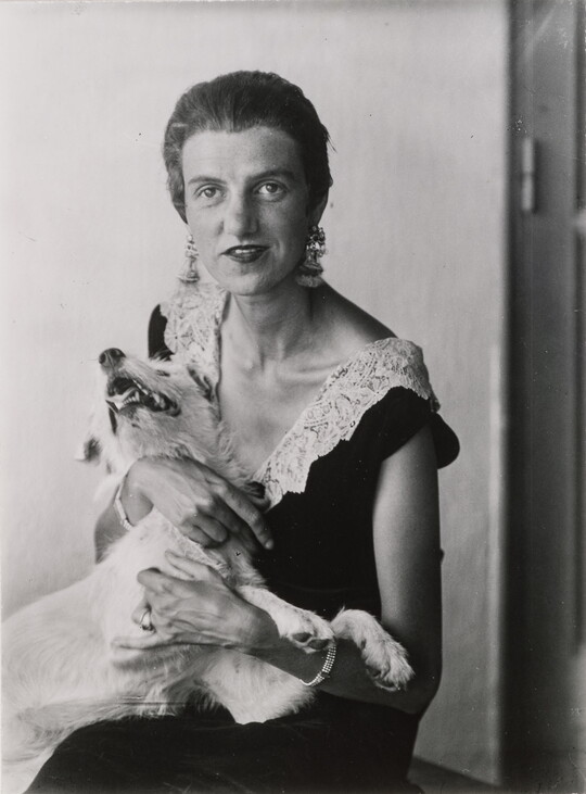 A black-and-white portrait photograph of a seated, nicely dressed White woman embracing a white dog.