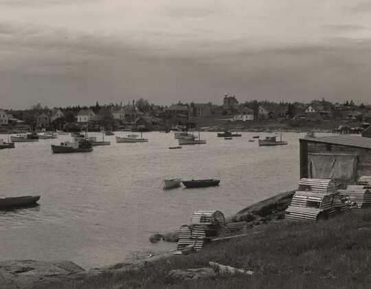 A black-and-white photograph of many fishing boats on calm water surrounded by houses on the shore.