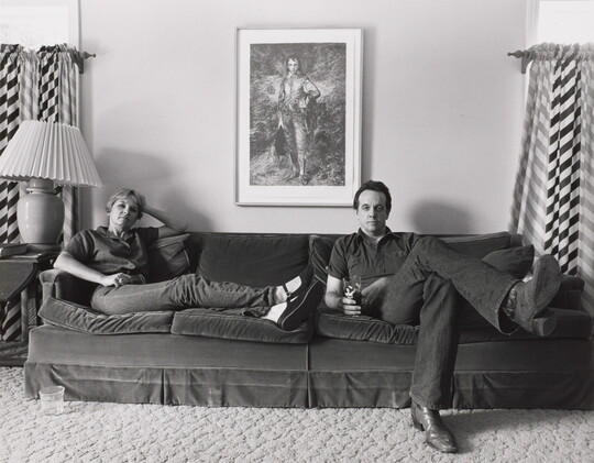 A black-and-white photograph of a White woman and man seated at opposite ends of a couch.