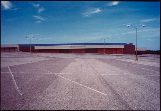 A color photograph of an abandoned strip mall and empty parking lot.
