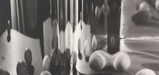 An abstract black-and-white photograph of blurred orb shapes reflected on a curved surface.