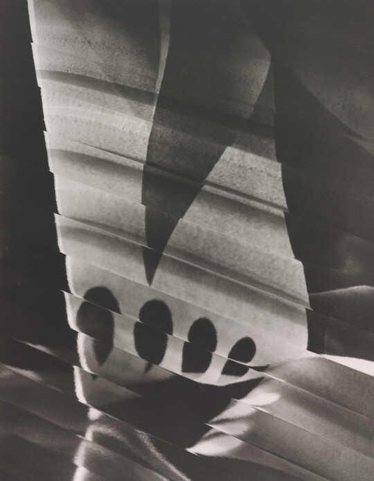 An abstract black-and-white photograph of a skewed white rectangular shape broken by a dark triangle, four tear-drop shapes, and lines.