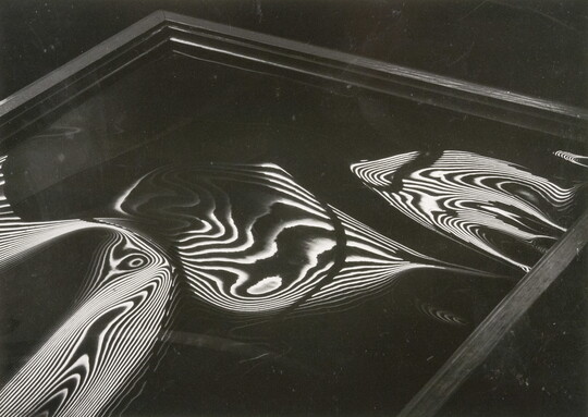 An abstract black-and-white photograph of a square-edged frame containing liquid-like organic round shapes with high-contrast nested contour lines.