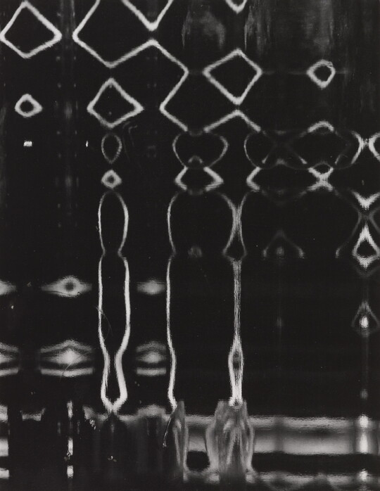 An abstract black-and-white photograph of white lines making a pattern of diamonds and drip-like shapes on a black background.