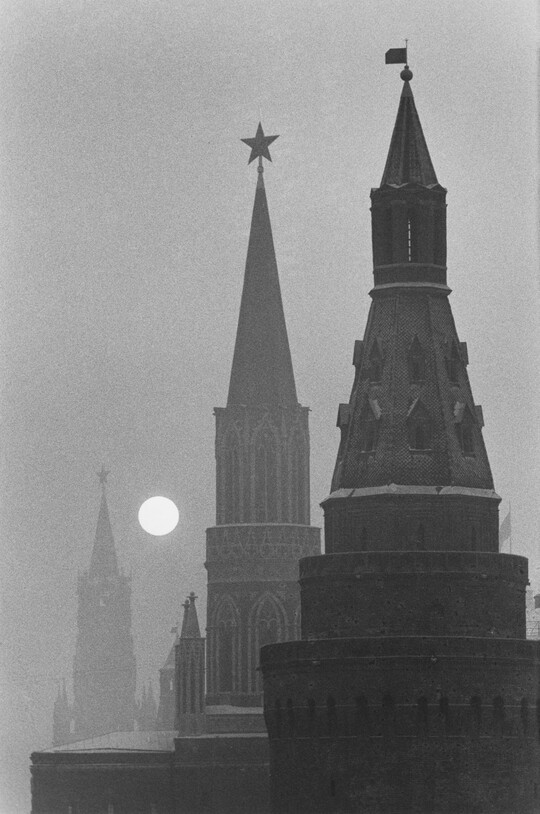 A black-and-white photograph of three spires fading into the distance with a bright, full moon rising.