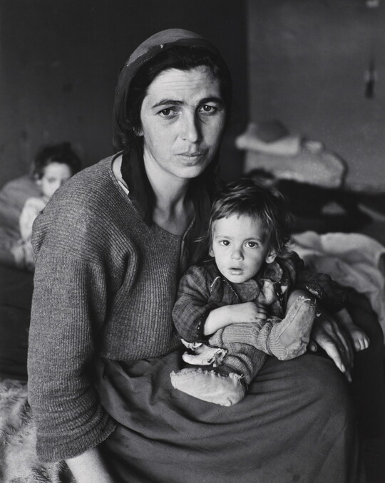A black-and-white photograph of a tired-looking White woman hunched over a small child in her lap.