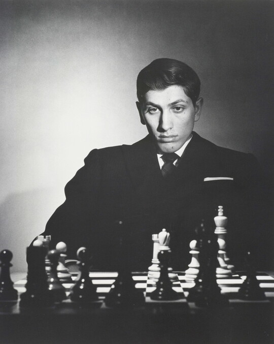 A black-and-white portrait photograph of a White man sitting and studying a chess board.