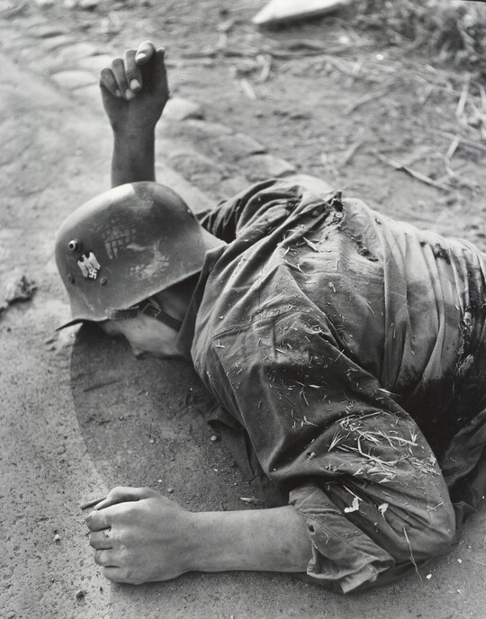 A black-and-white photograph of a deceased, White soldier laying facedown on a road.