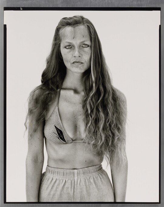 A black-and-white portrait photograph of a White woman with long hair, wearing a bikini top and athletic shorts.