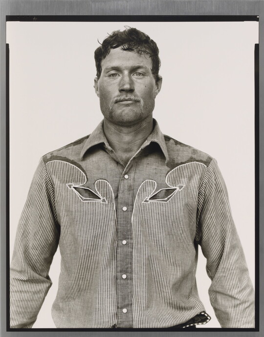 A black-and-white portrait photograph of a White man, with short hair and light facial hair, wearing a button-down shirt with Western details.