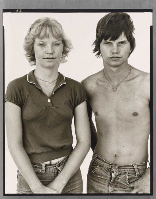 A black-and-white portrait photograph of a young White woman with short blonde hair and a shirtless, young White man with short tousled hair.