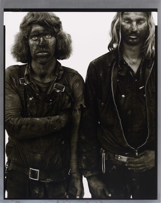 A black-and-white portrait photograph of two men standing side by side, both covered in dark coal dust.