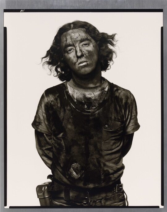 A black-and-white portrait photograph of a young man with curly hair covered in dark coal dust.