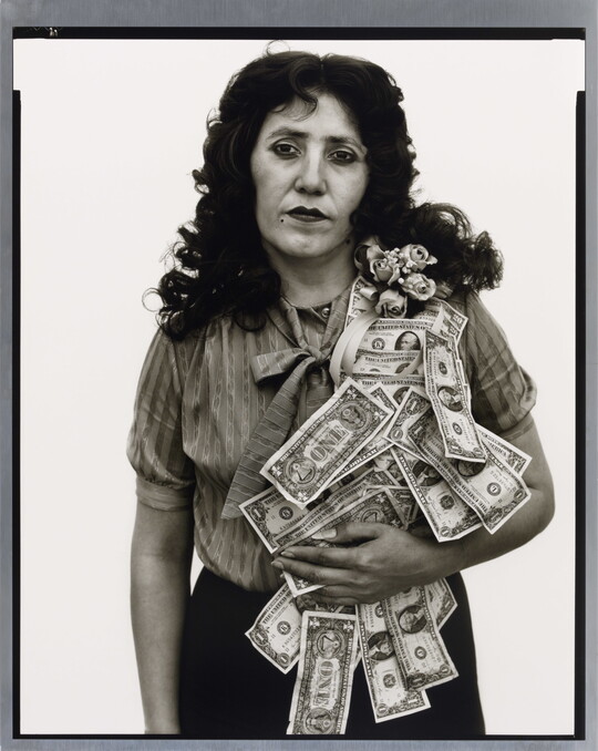 A black-and-white portrait photograph of a White woman with a sash of flowers and dollar bills flowing over her shoulder.