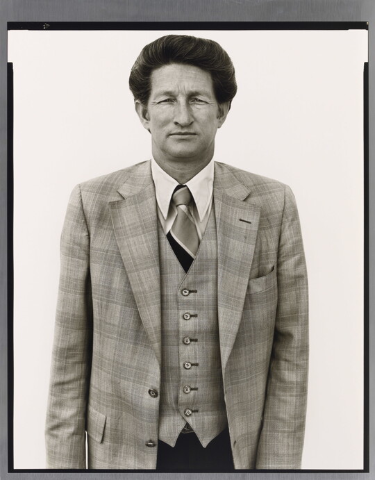 A black-and-white portrait photograph of a dark-haired, White man wearing a three-piece plaid suit with a tie.