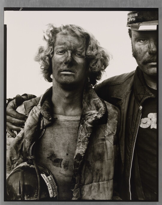 A black-and-white portrait photograph of two men, one with his arm around the other, both covered in coal dust and wearing dirty clothes.