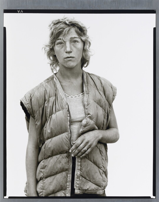 A black-and-white portrait photograph of a young White woman with short wavy hair wearing a puffer vest looking straight at the viewer.