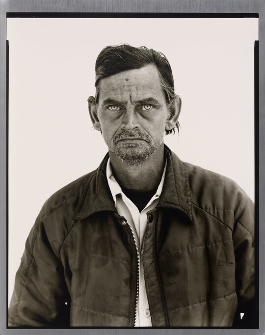 A black-and-white portrait photograph of a White man with a salt-and-pepper goatee wearing a collared shirt under a quilted jacket.
