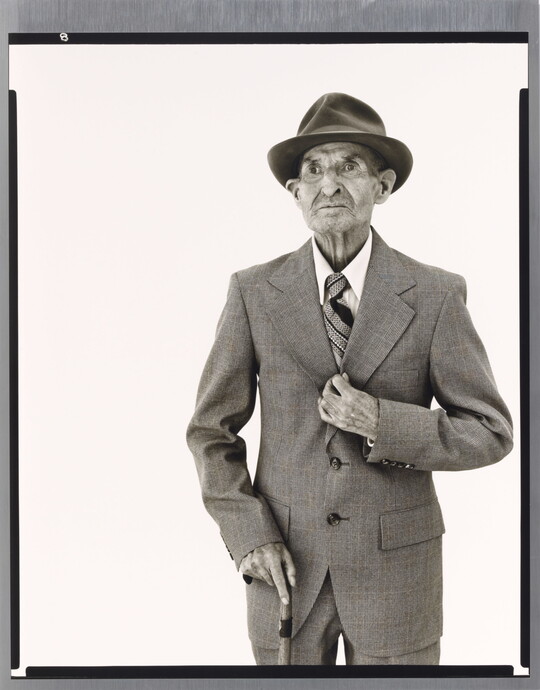 A black-and-white portrait photograph of an elderly White man in a hat, suit, tie, and one hand holding a cane.