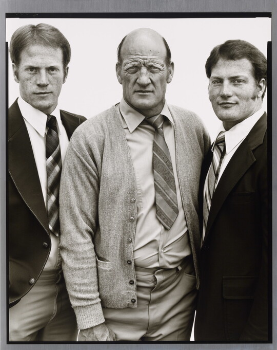 A black-and-white portrait photograph of three White men, two younger on the left and right and the one in the center middle-aged and bald, all wearing suits and ties.