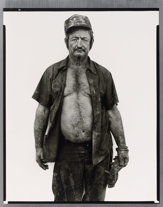 A black-and-white portrait photograph of a middle-aged White man wearing a baseball cap, a dirty, open button-down shirt, and a work glove on one hand.