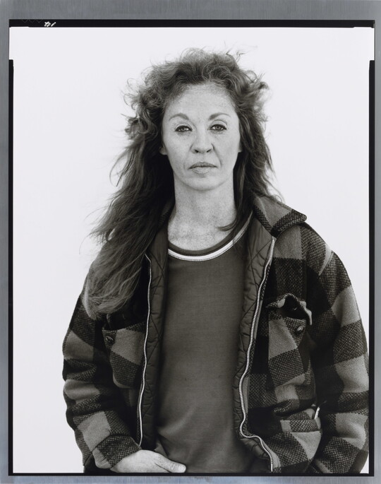 A black-and-white portrait photograph of a middle-aged White woman with long hair wearing a checked jacket.