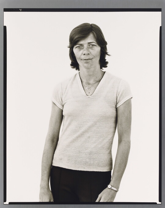 A black-and-white portrait photograph of a White woman with short hair, wearing a light V-neck shirt and dark pants.