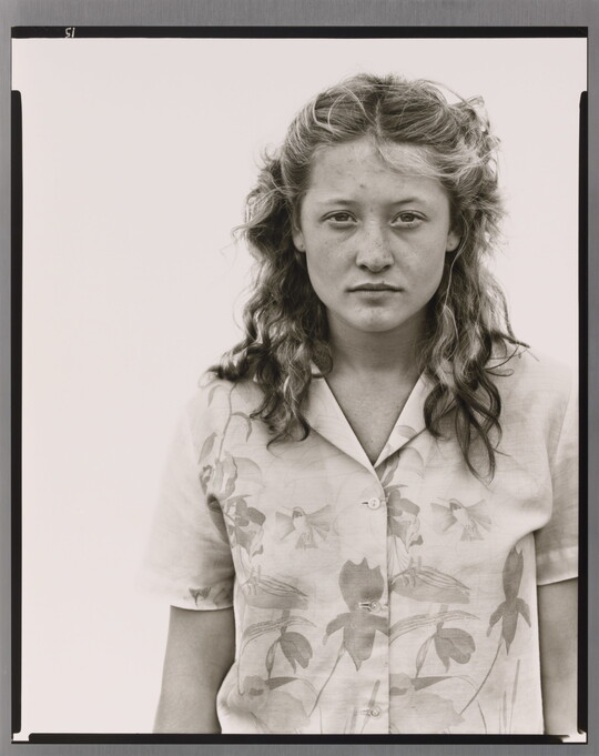 A black-and-white portrait photograph of a White teenage girl with her blonde hair pulled back in barrettes and wearing a floral button-up blouse.