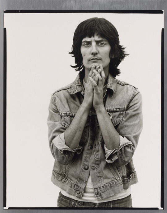 A black-and-white portrait photograph of a light-skinned woman wearing a denim jacket and holding her hands together up to her chin.