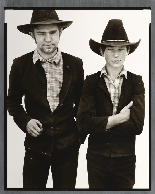 A black-and-white portrait photograph of a young White man and boy, both wearing cowboy hats, dark jackets, and plaid shirts.