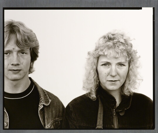 A black-and-white portrait photograph of a young White man with shaggy hair wearing a jean jacket, and a young White woman with curly hair wearing a corduroy jacket.