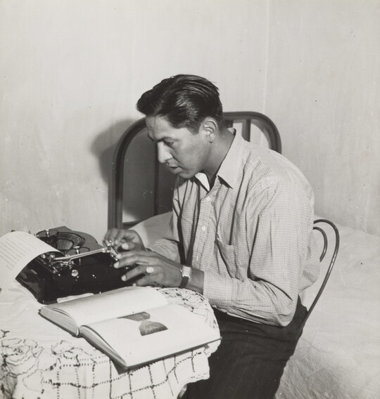 A black-and-white photograph of a Native American man typing on a typewriter.