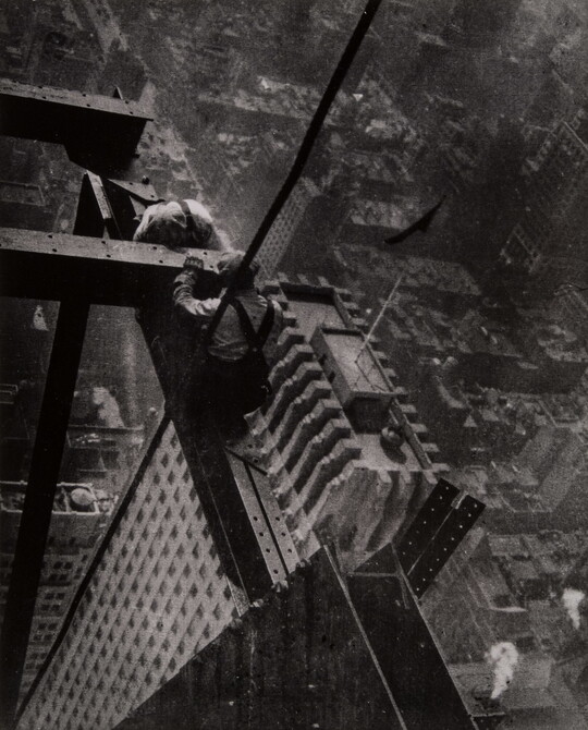 A black-and-white photograph of two men bent over their work atop steel beams high above the skyscrapers of a city.