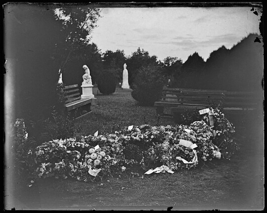 A black-and-white image of a cemetery with a grave completely covered in fresh flowers in the foreground.